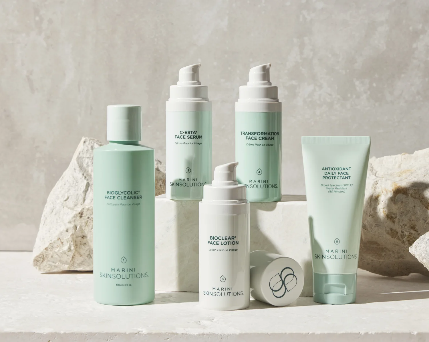 Sage-green Marini Skin Care Management System products arranged among pale sculptural stones